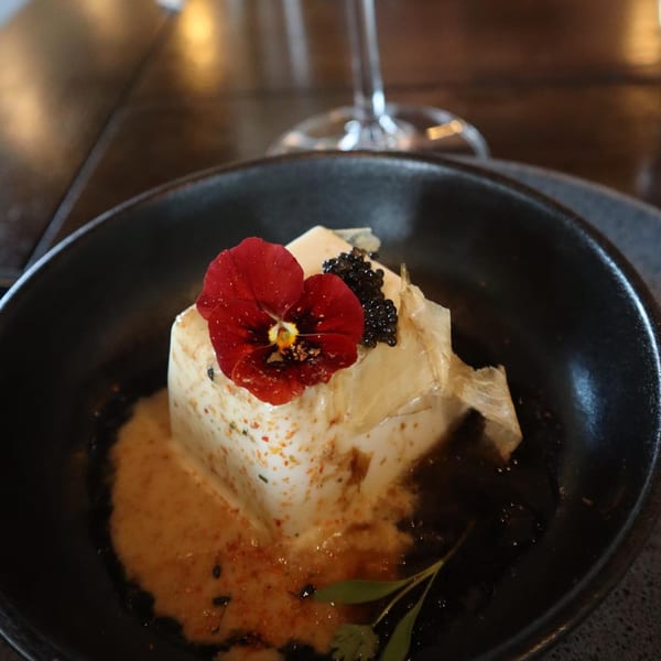 A Vietnamese dish with a white square of food topped with a red flower and black caviar.