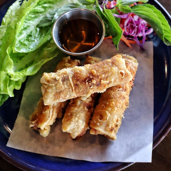 Crispy Vietnamese spring rolls with lettuce, herbs, and dipping sauce on a blue plate.