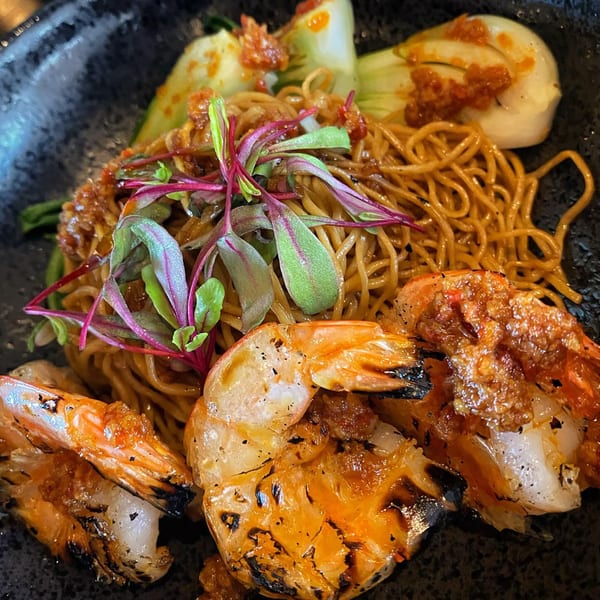 Grilled shrimp and noodles with bok choy and microgreens, served in a dark bowl at Saigon District.