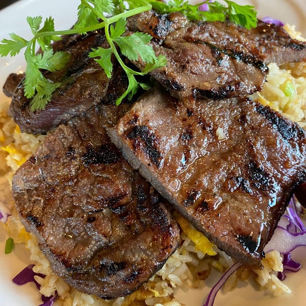 Grilled beef slices with cilantro on a bed of fried rice and purple cabbage.