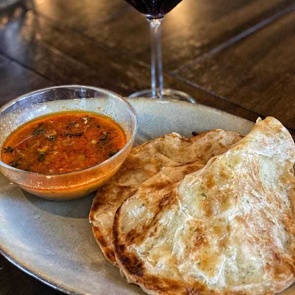 Two crispy Vietnamese flatbreads with a side of red curry sauce and a glass of wine.
