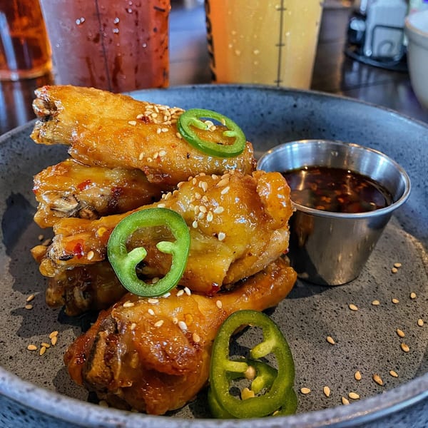 Crispy Saigon District chicken wings with sesame seeds, jalapeños, and dipping sauce on a dark plate.