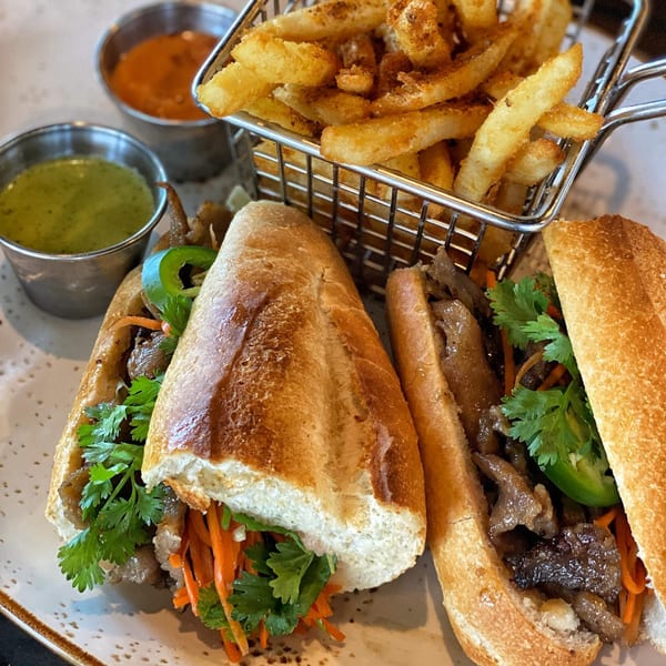 Two Vietnamese banh mi sandwiches with fries and dipping sauces on a plate.