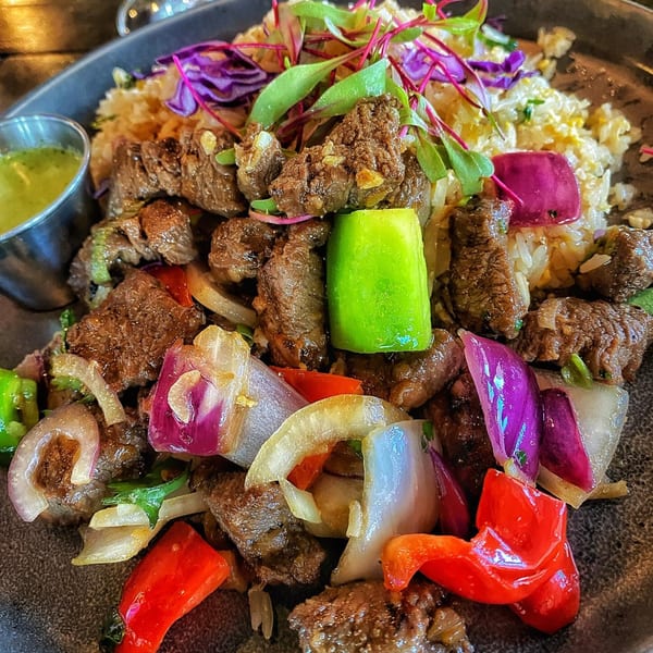 Shaking beef with rice, red and green bell peppers, onions, and a side of green sauce.