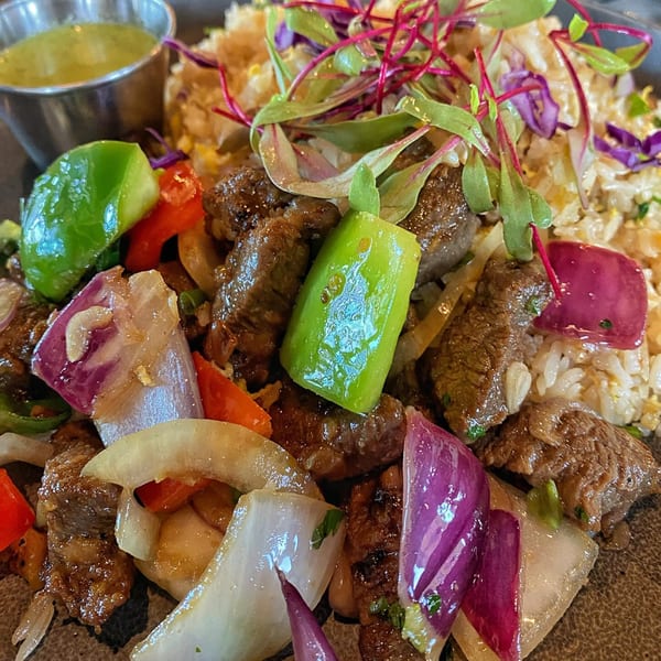 Close-up of Vietnamese shaking beef with bell peppers, onions, and rice, served with a green dipping sauce.
